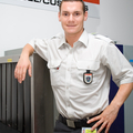Auf dem Bild ist ein Zollner in einer Zolluniform vor einem Gepäckscanner zu sehen.