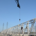 Das Bild zeigt eine industrielle Wasseraufbereitungsanlage, in der eine Fachkraft auf einer metallenen Wartungsbrücke mit einem Kran über einem Klärbecken arbeitet.