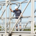 Ein Abwassertechniker in Sicherheitsausrüstung arbeitet an einer Wasseraufbereitungsanlage. Er steht auf einer metallenen Wartungsbrücke über einem Klärbecken und arbeitet an der Wartung.