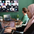 Auf dem Bild sind zwei ApplikationsentwicklerInnen zu sehen; die Person im Vordergrund arbeitet an einem Laptop, während die andere Person aktiv an einem virtuellen Meeting teilnimmt.