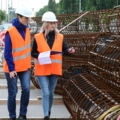 Zwei bautechnische Assistentinnen in Sicherheitswesten und Helmen inspizieren Baustahl auf einer Baustelle.