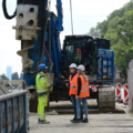 Auf dem Bild sind bautechnischen AssistentInnen in Schutzkleidung zu sehen, die auf einer Baustelle bei einem großen Bohrgerät stehen und sich unterhalten.