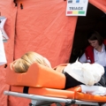 Das Bild zeigt eine medizinische Notfalltriage-Situation, bei der eine Person auf einer Trage von SanitäterInnen betreut wird.