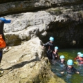 Ein Guide in Neoprenanzug und Helm führt eine Gruppe von Menschen beim Canyoning durch eine felsige Wasserlandschaft.