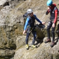 Auf dem Bild sind zwei CanyonführerInnen in Kletterausrüstung und Helmen bei Outdoor-Aktivitäten zu sehen.