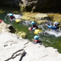 Auf dem Bild sind Personen mit Helmen und Neoprenanzügen beim Canyoning in einem Fluss zu sehen.