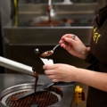 Eine Chocolatières arbeitet in einer Schokoladenmanufaktur und füllt Schokolade in einen Behälter.