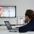 Ein Creative Director sitzt an einem Tisch und schaut auf einen Laptop und einen Bildschirm, die eine Grafik zeigen.