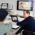In einem modernen Büro besprechen zwei Creative Directors an einem Tisch Inhalte auf einem Laptop und einem Bildschirm.