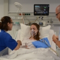 In dem Bild kümmern sich diplomierte Gesundheits- und KrankenpflegerInnen um eine Patientin in einem Krankenhausbett.