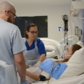 Das Bild zeigt diplomierte Gesundheits- und KrankenpflegerInnen, welche sich um eine Patientin in einem Krankenhausbett kümmern.