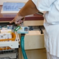 Eine Diplomierte Gesundheits- und KrankenpflegerIn in medizinischer Kleidung zeigt auf eine Schublade mit Medikamenten in einem Krankenhaus.