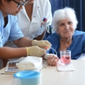 Auf dem Bild sind zwei diplomierte Gesundheits- und Krankenpflegerinnen zu sehen, die eine medizinische Behandlung an einer ältere Person durchführen.