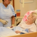 Eine diplomierte Gesundheits- und Krankenpflegerin kümmert sich um eine ältere Patientin in einem Krankenbett.