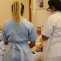 Das Bild zeigt zwei diplomierte Gesundheits- und Krankenpflegerinnen in Arbeitskleidung, die sich um eine pflegebedürftige Person kümmern.