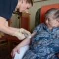 Eine diplomierte Gesundheits- und Krankenpflegerin versorgt den Arm einer älteren Frau mit einem Verband.