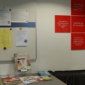 Das Bild zeigt das Büro des Roten Kreuzes mit Informationsmaterial und Anschlagtafel.