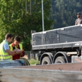 Zwei Baumarktverkäufer in Sicherheitswesten besprechen sich neben einem Lastwagen, während ein Lieferant von neuen Produkten auf der Ladefläche steht.