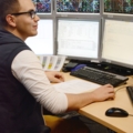 Auf dem Bild ist ein Eisenbahnbetriebstechniker zu sehen, der an einem Computerarbeitsplatz mit mehreren Bildschirmen arbeitet, auf denen technische Diagramme und Daten angezeigt werden.