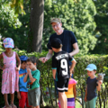 Auf dem Bild beaufsichtigt und interagiert ein Elementarpädagoge mit mehreren spielenden Kinder im Freien.