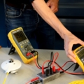 Auf dem Bild sind ElektroenergietechnikerInnen zu sehen, die mit Multimetern elektrische Messungen durchführen.