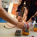 Auf dem Bild sind ElektroenergietechnikerInnen zu sehen, die mit Multimetern und Kabeln elektrische Messungen durchführen.
