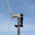 Ein Elektroenergietechniker in Arbeitskleidung mit Schutzhelm führt Wartungsarbeiten an einem Windrad durch.
