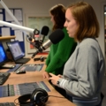 Das Bild zeigt zwei Medienmanagement-Studierende, die in einem Fernsehstudio vor Mikrofonen und Computern stehen.
