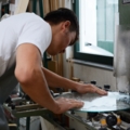 Ein Glasbautechniker bearbeitet in einer Werkstatt eine Glasscheibe an einer Maschine.