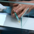 Ein Glasbautechniker trägt mit einer Spritze Klebstoff auf Glas auf.