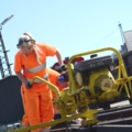 Eine Gleisbautechnikerin in Sicherheitskleidung arbeitet mit einer Maschine an Eisenbahnschienen.