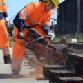 Eine Gleisbautechnikerin in Sicherheitskleidung schneidet mit einem Trennschleifer einen Eisenbahnschienenstrang.