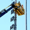 Auf dem Bild sind GleisbautechnikerInnen in einer Hebebühne zu sehen, die an einer hohen Konstruktion arbeiten.