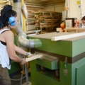 Zwei Zimmerinnen arbeiten in einer Schreinerei, wobei sie eine Maschine zur Holzbearbeitung verwenden.