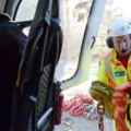 Das Bild zeigt einen Piloten in Schutzkleidung, der in einem Hubschrauber arbeitet und mit Seilen hantiert.