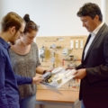 Ein Immobilienkaufmann erklärt zwei Lehrlingen verschiedene Geräte der Haustechnik.