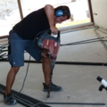 Ein Installations- & Gebäudetechniker benutzt einen Bohrhammer, um Löcher in einen Betonboden zu bohren.