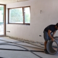 Zwei Installations- & Gebäudetechniker verlegen Kabel und Rohre in einem unvollendeten Raum.