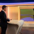 Auf dem Bild ist ein Nachrichtenmoderator in einem Fernsehstudio zu sehen.