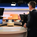 Ein Fernsehmoderator steht in einem Studio mit Kameras und Teleprompter.