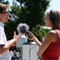 Auf dem Bild ist eine Journalistin mit Kopfhörern und einem Mikrofon zu sehen, die ein Interview mit einem Mann führt.