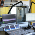 Das Bild zeigt ein Radiostudio mit Mischpult und Bildschirmen.