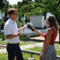 Auf dem Bild ist eine Journalistin zu sehen, die ein Interview im Freien führt.