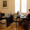 Zwei investigative Journalisten arbeiten in einem Büro an ihren Schreibtischen; einer liest, während der andere am Computer arbeitet.