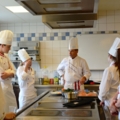 Auf dem Bild sind Köche in einer professionellen Küche bei einer Schulung zu sehen.