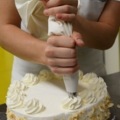 Auf dem Bild dekoriert eine Konditorin eine Torte mit Sahne.