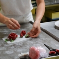 Eine Konditorin dekoriert eine Torte mit kunstvoll geformten Zuckerröschen in einer Konditorei.