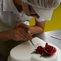 Eine Konditorin dekoriert eine herzförmige Torte mit essbaren roten Rosen und verziert sie mit feinen Details.