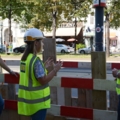 Auf dem Bild sind Kran- und BaumaschinenführerInnen in Warnwesten und Helmen auf einer Baustelle zu sehen, die miteinander sprechen.
