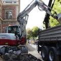 Ein Bagger hebt Schutt auf eine Baustelle und lädt ihn in einen Lastwagen.